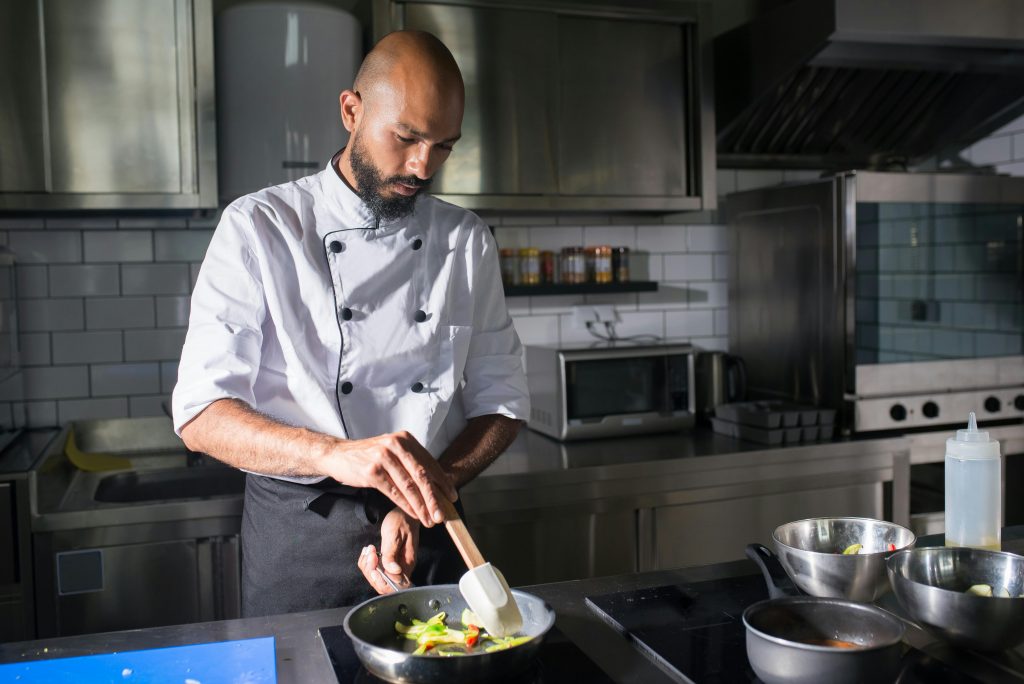 Home A skilled chef prepares fresh vegetables in a frying pan in a well-equipped kitchen.