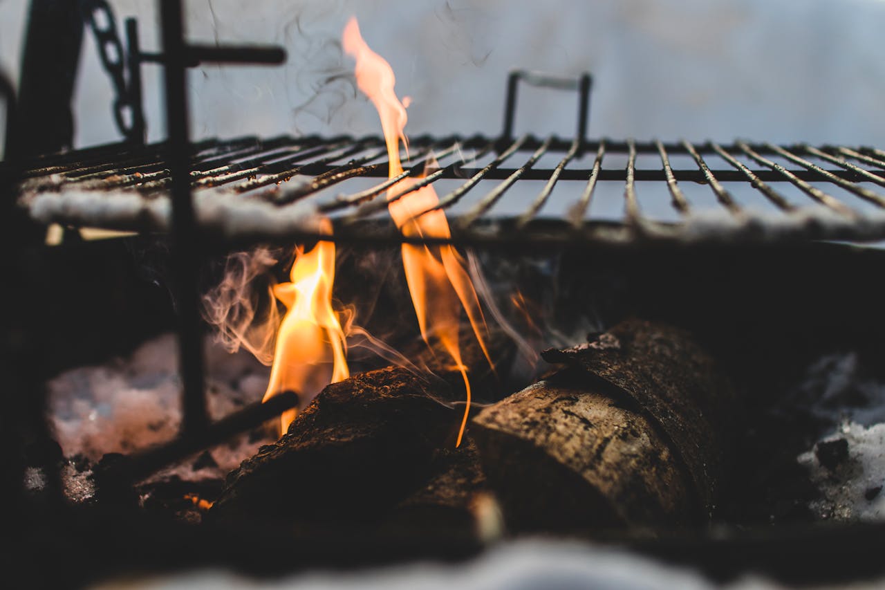pexels-photo-983373 Close-up view of firewood burning in a fire pit with a metal grill above, outdoor setting.
